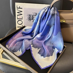 Elegant silk scarf with blue floral patterns draped over a stylish leather handbag