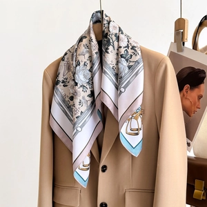 Elegant floral twill silk scarf with equestrian elements draped on a beige blazer collar
