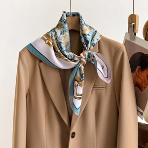 Floral twill silk scarf with teal and mustard patterns tied on a khaki blazer