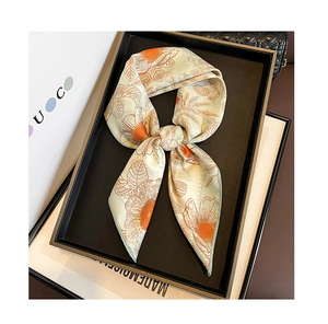 Détail d'un foulard en soie à fleurs orange à côté d'un sac à main matelassé