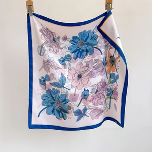 Elegant floral square silk scarf in pink and blue, vertically hanging on a white wall