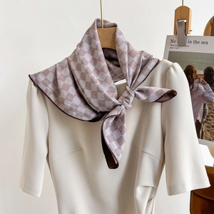 Élégant foulard en soie à damier café et beige noué sur l'encolure d'une robe