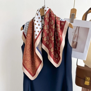 Double-sided paisley print silk scarf styled on a hanger with blue dress and leather bag