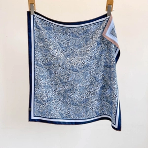 Blue paisley silk square scarf with contrasting border hanging against white background