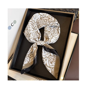 Detail of silk scarf with rose print and black trim draped over a luxury handbag