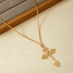 Gros plan du pendentif croix dorée vintage avec motif floral évidé et strass central