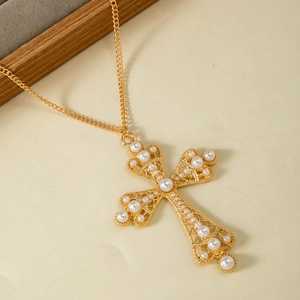 Détail du pendentif croix dorée vintage ajourée orné de perles blanches élégantes