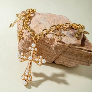 Dettaglio di una collana a croce dorata vintage con perle e strass su pietra naturale
