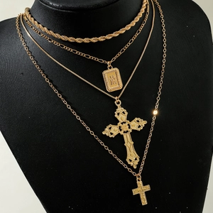 Detail of layered gold cross necklace with rectangular embossed pendant and mixed chains