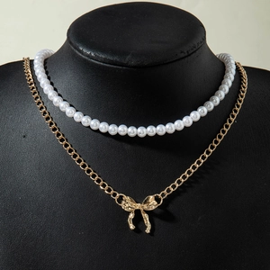 Détail du collier double rang avec perles blanches et pendentif nœud doré élégant