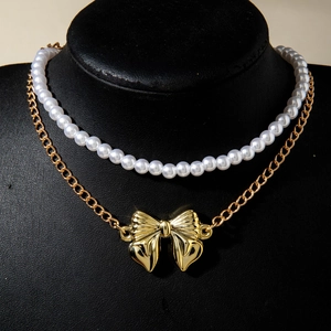 Détail du collier double rang avec perles blanches et pendentif nœud doré sur support