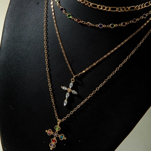 Macro shot of layered gold cross necklaces with vibrant multi-color crystal inlay