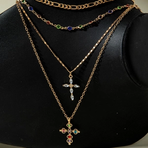 Layered gold cross necklace set with colorful rhinestones on a black display stand