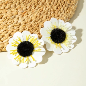Detail of white daisy earrings with yellow stamens on a textured woven background
