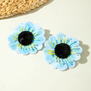 Close-up of light blue sunflower earrings with yellow stamens and woven straw background