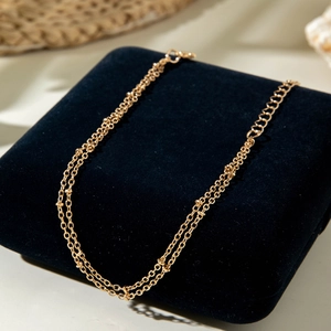 Detail of a gold double-layer chain anklet with delicate beads on blue velvet jewelry box