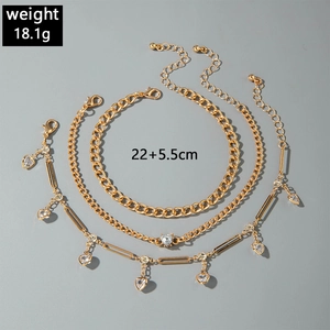 Close-up of gold tiered anklets with snake chain and heart rhinestone pendant details