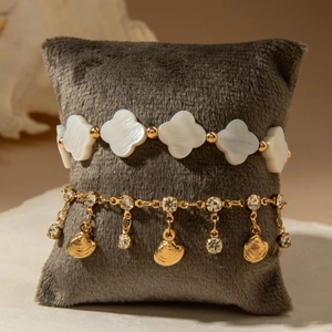 Detail of layered gold anklets featuring clover shell beads and seashell pendants