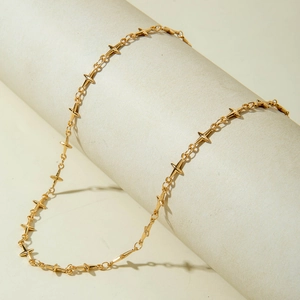 Gros plan d'un collier croix doré multicouche drapé sur un support beige cylindrique