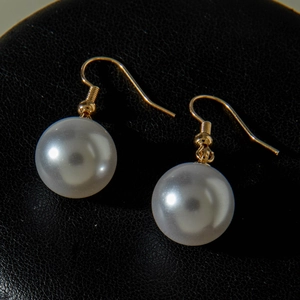 Close-up of elegant round pearl earrings with gold hooks on black leather background