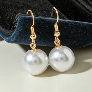 Detailed close-up of white pearl drop earrings with gold hooks on navy velvet display