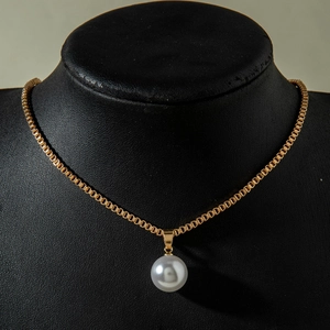 Détail d'un pendentif en perle blanche sur une chaîne dorée et buste noir élégant