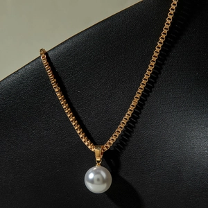 Détail d'un pendentif en perle blanche sur une chaîne box dorée sur fond de cuir noir