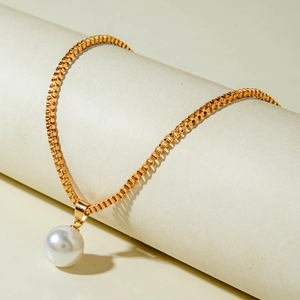 Détail d'un pendentif perle blanche sur chaîne box dorée drapé sur un rouleau minimaliste