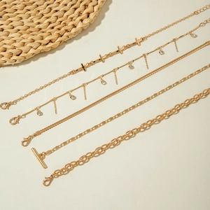 Five-piece gold layered anklet set featuring cross charms, rhinestones, and chunky OT buckle
