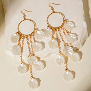 Details langer goldener Quastenohrringe mit schillernden Muschel-Anhängern auf Stein
