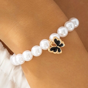 Détail d'un bracelet en perles avec un élégant pendentif papillon noir et doré au poignet
