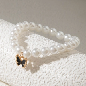 Détail d'un bracelet en perles blanches avec pendentif papillon en émail noir sur son support