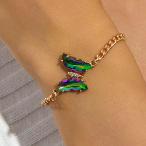 Détail d'un bracelet papillon doré avec des ailes irisées et des accents de diamants blancs