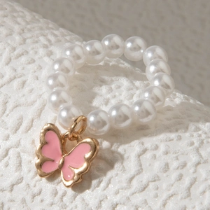 Gros plan d'une bague en perles avec pendentif papillon en émail rose sur pierre