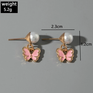 Détail des boucles d'oreilles papillon roses avec perles blanches et émail doré