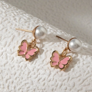 Gros plan de boucles d'oreilles papillon en émail rose avec perles et bord doré