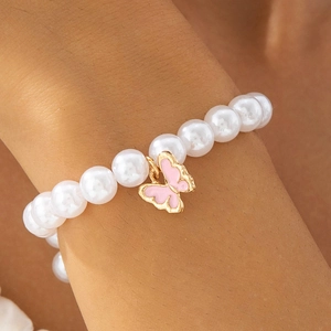 Détail d'un bracelet en perles blanches avec pendentif papillon en émail rose et doré