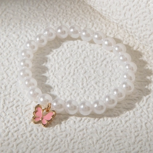 Détail du bracelet en perles avec pendentif papillon rose émaillé sur surface texturée