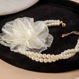 Detail of double-layer white faux pearl necklace featuring a large organza flower accent