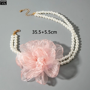 Close-up of white pearl necklace with large pink fabric flower and golden clasp details