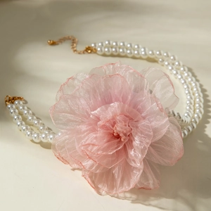 Macro view of double-layered white faux pearl necklace with large pink organza flower