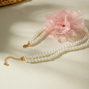 Detail of double-layer pearl necklace featuring a delicate pink organza flower and gold clasp