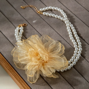 Detail of double-layer pearl necklace with a large golden organza flower decoration