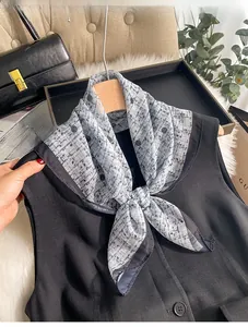 Close-up of a 70cm grey geometric chiffon scarf styled on a black vest with props