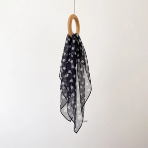 Detail of dark blue chiffon scarf with white floral patterns draped through a wooden ring