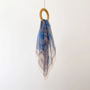 Elegant blue and white Paisley silk scarf hanging through a wooden ring on white background