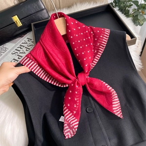 Dettaglio foulard in seta rossa a pois bianchi indossato su un gilet nero