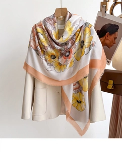 Detailed view of floral silk scarf with tassels layered over a beige blazer and leather bag