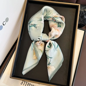 Detail shot of the light green floral silk scarf tied in an elegant knot on a luxury tray