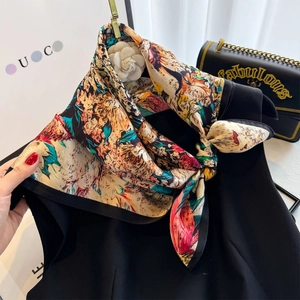 Close-up of printed silk square scarf styled with a white camellia brooch and gold chain bag